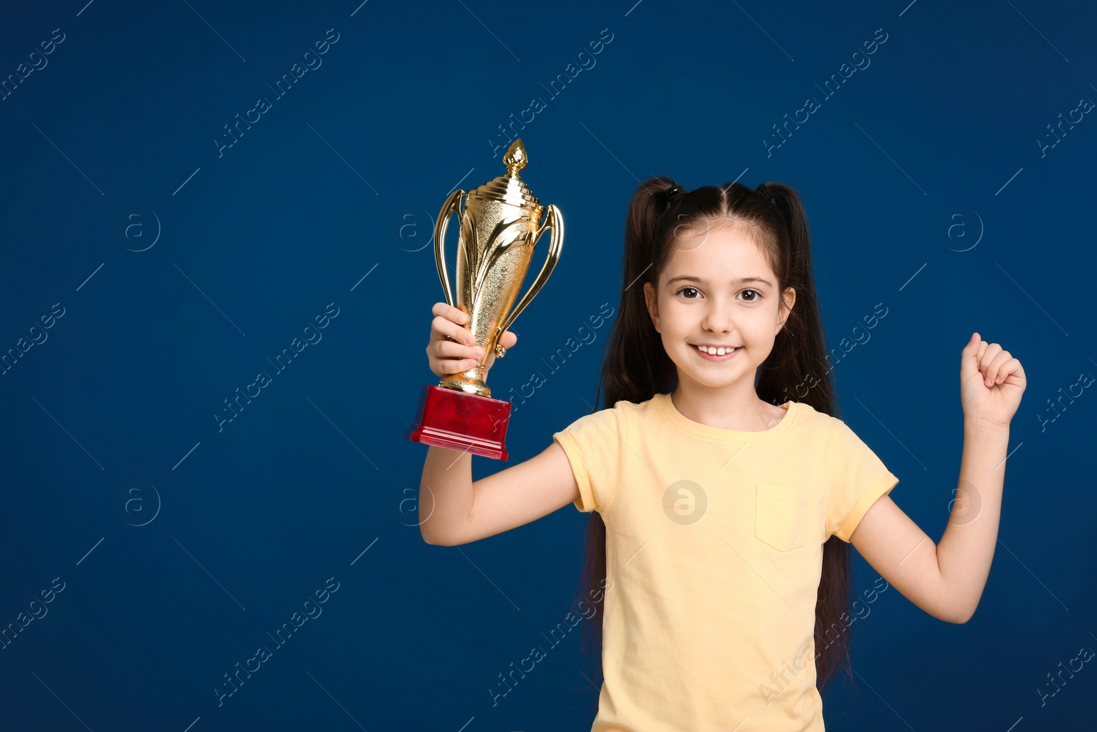 Photo of Happy girl with golden winning cup on dark blue background. Space for text