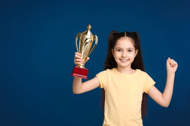 Photo of Happy girl with golden winning cup on dark blue background. Space for text