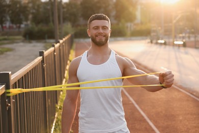 Photo of Muscular man doing exercise with elastic resistance band outdoors at sunset