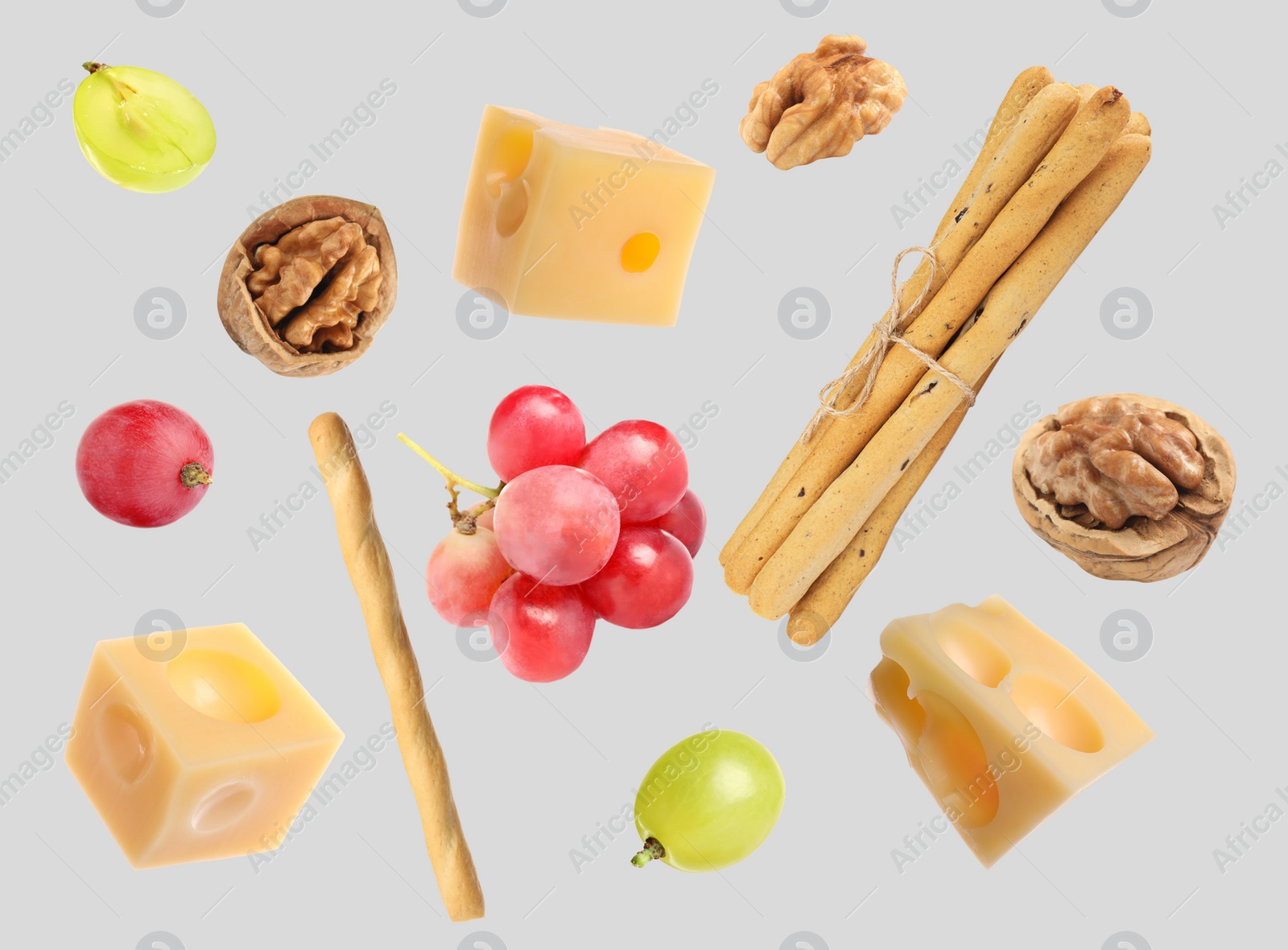 Image of Cheese, breadsticks, grapes and walnuts falling against light grey background