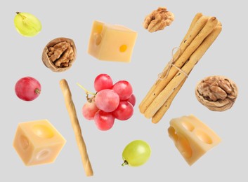 Image of Cheese, breadsticks, grapes and walnuts falling against light grey background