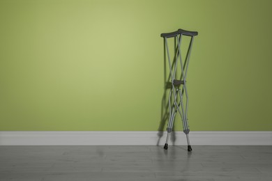 Pair of axillary crutches near light green wall. Space for text
