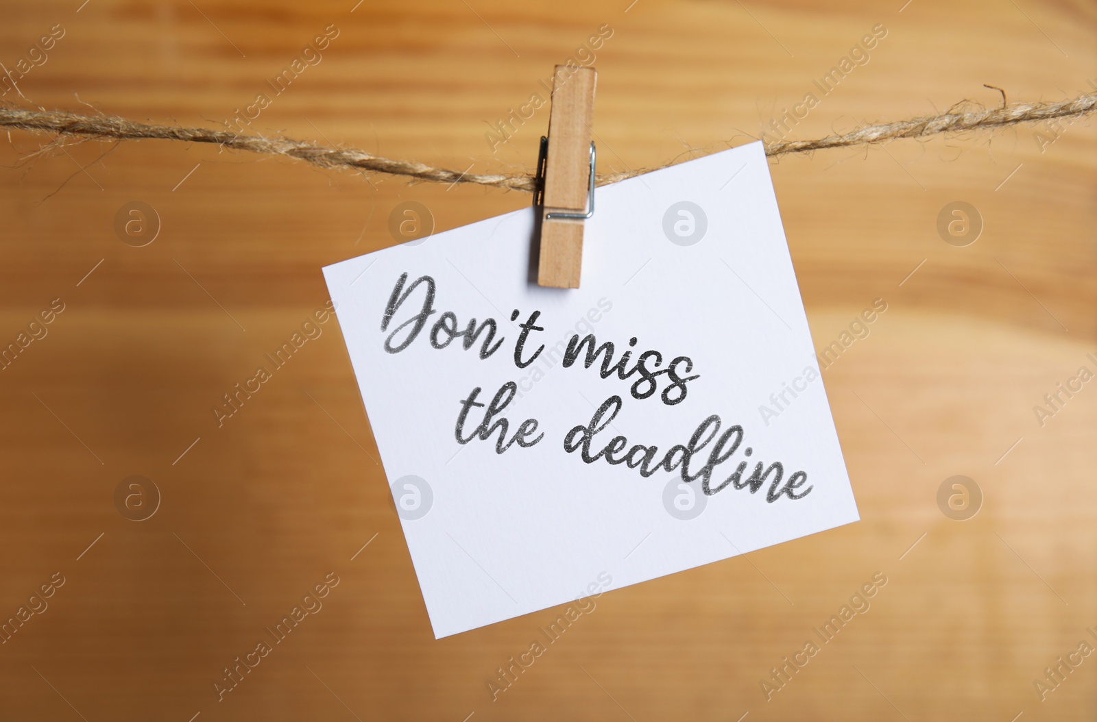 Image of Note with reminder Don't Miss The Deadline hanging on twine against wooden background