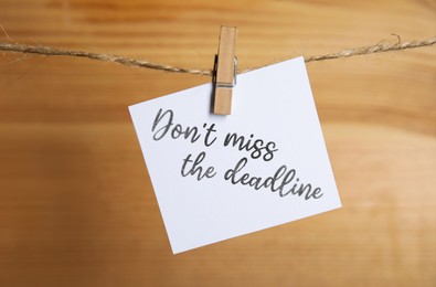 Note with reminder Don't Miss The Deadline hanging on twine against wooden background
