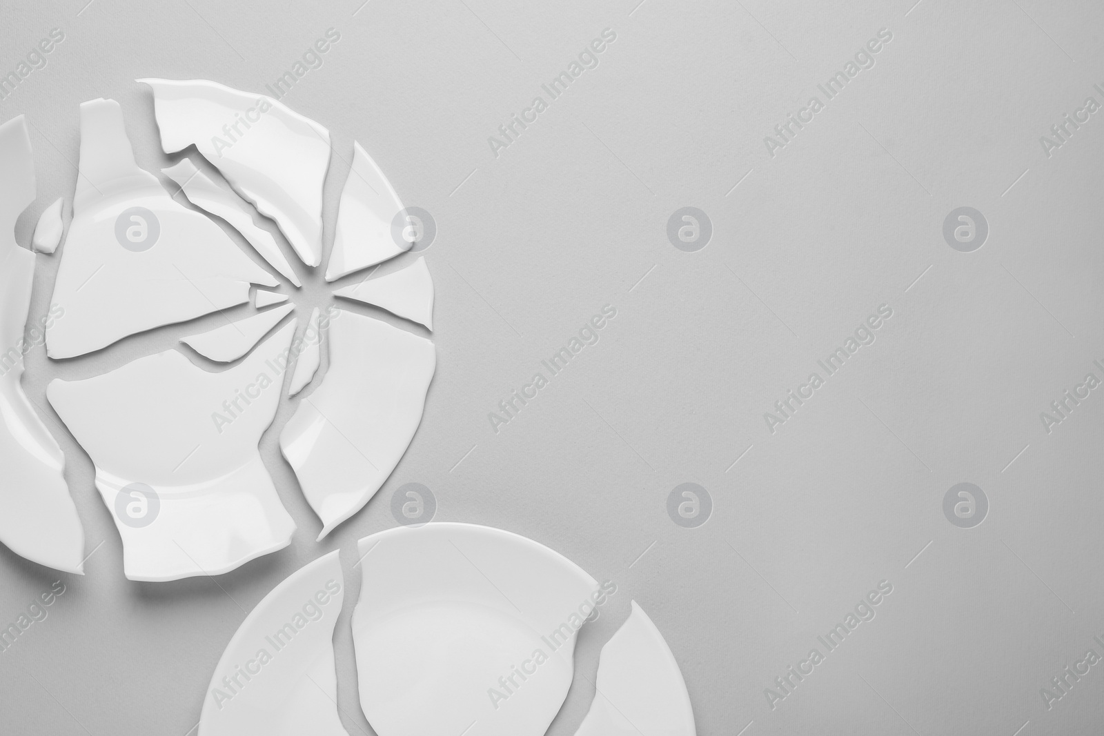 Photo of Two broken ceramic plates on light grey background, flat lay. Space for text