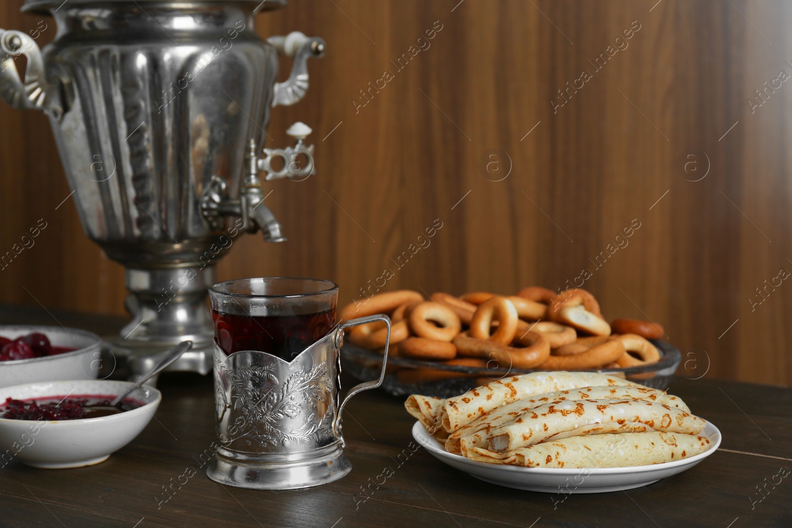 Photo of Vintage samovar, cup of hot drink and snacks served on wooden table. Traditional Russian tea ceremony