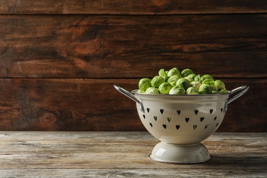 Photo of Colander with Brussels sprouts on wooden background. Space for text