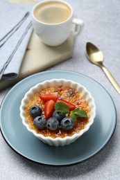 Photo of Delicious creme brulee with berries and mint in bowl served on grey textured table