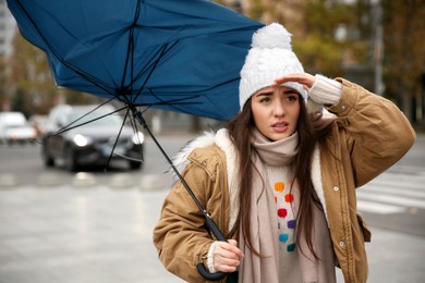 Photo of Woman with blue umbrella caught in gust of wind on street