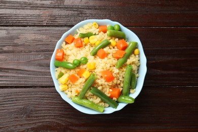 Photo of Delicious bulgur with vegetables in bowl on wooden table, top view