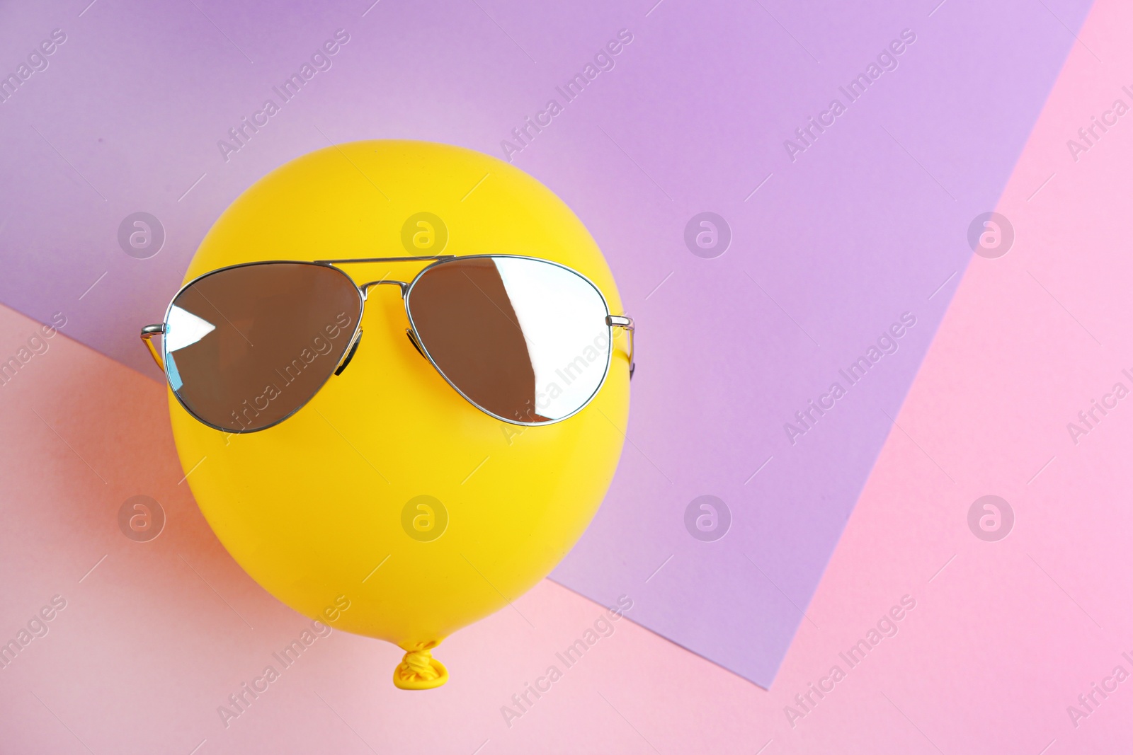 Photo of Funny face made of yellow balloon with sunglasses on color background, space for text