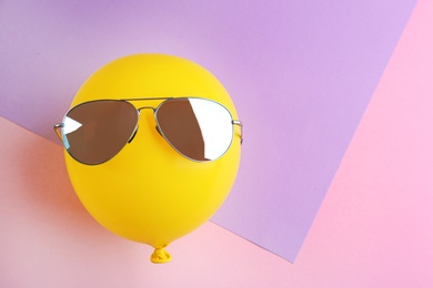 Funny face made of yellow balloon with sunglasses on color background, space for text