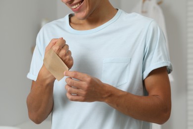 Photo of Man putting sticking plaster onto hand indoors, closeup