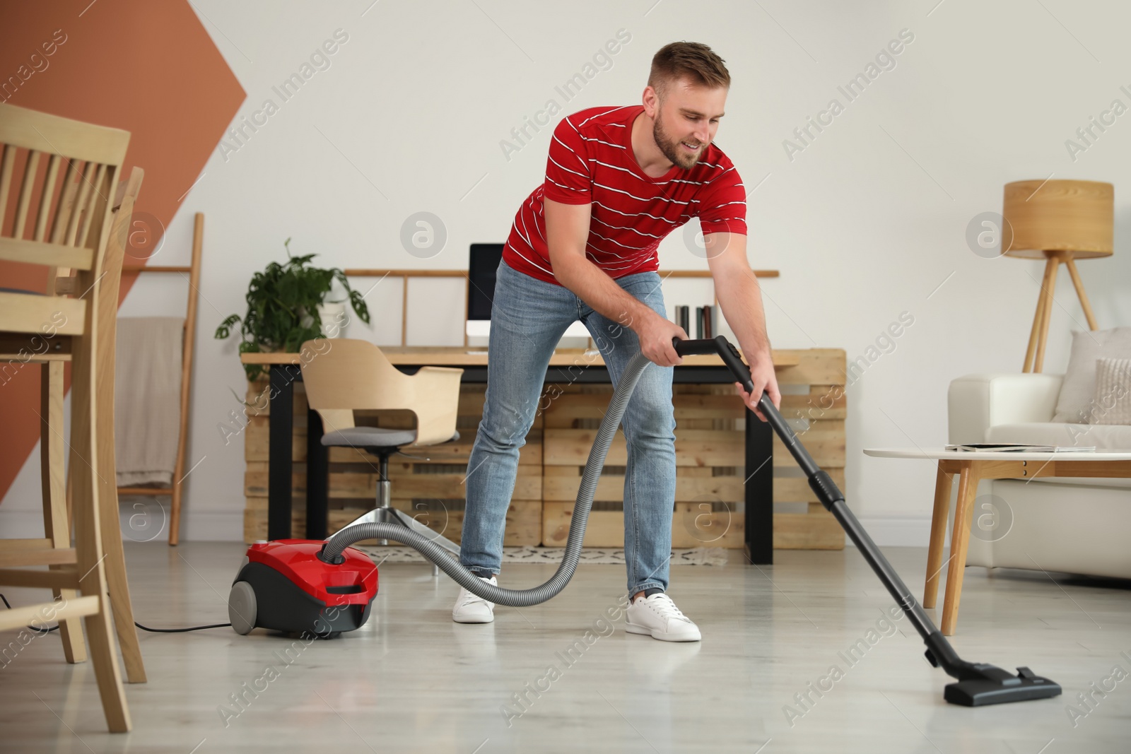 Photo of Young man using vacuum cleaner in living room