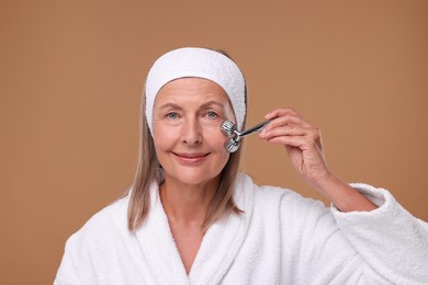 Woman massaging her face with metal roller on brown background