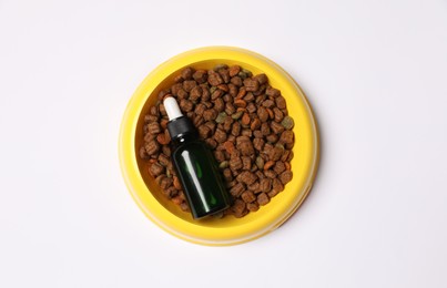 Glass bottle of tincture and dry pet food in bowl on white background, top view