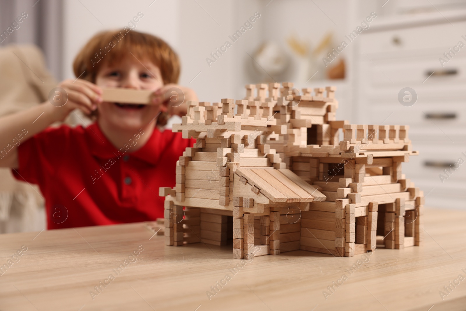 Photo of Cute little boy playing with wooden castle at table in room, selective focus. Child's toy