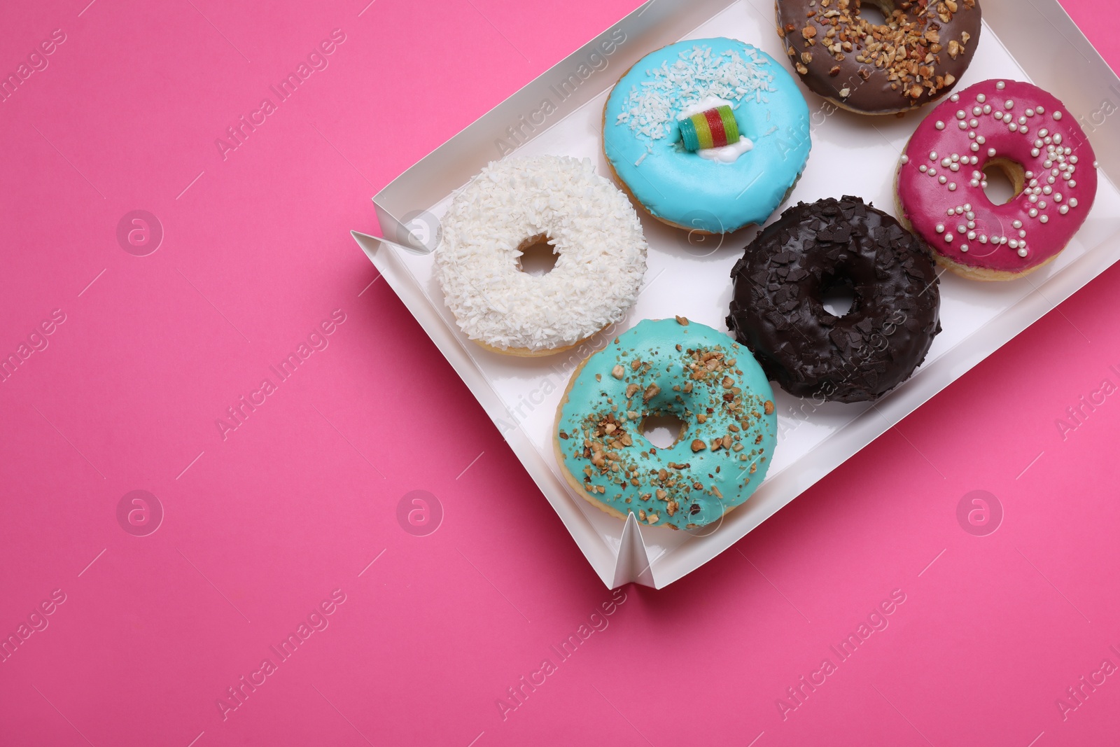 Photo of Box with different tasty glazed donuts on pink background, top view. Space for text