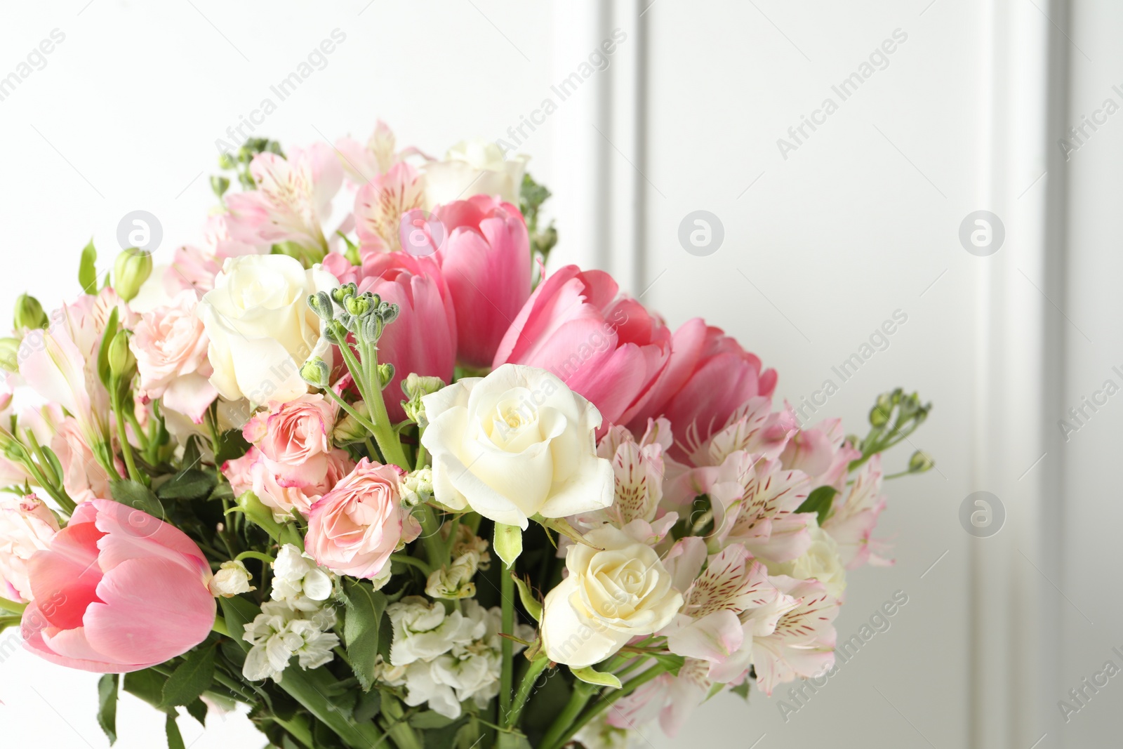 Photo of Beautiful bouquet of fresh flowers near white wall, closeup