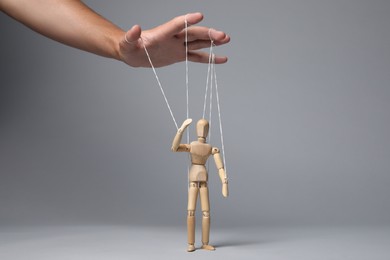Photo of Man pulling strings of puppet on gray background, closeup