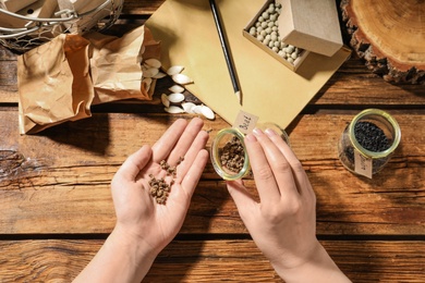 Photo of Woman with vegetable seeds at wooden table, top view