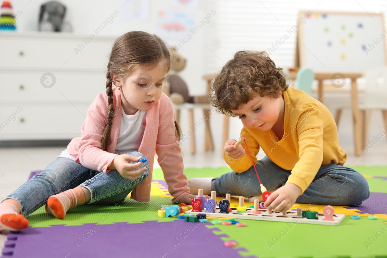 Photo of Cute little children playing with math game Fishing for Numbers on puzzle mat in kindergarten