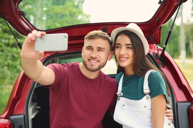 Photo of Beautiful young couple taking selfie in car trunk