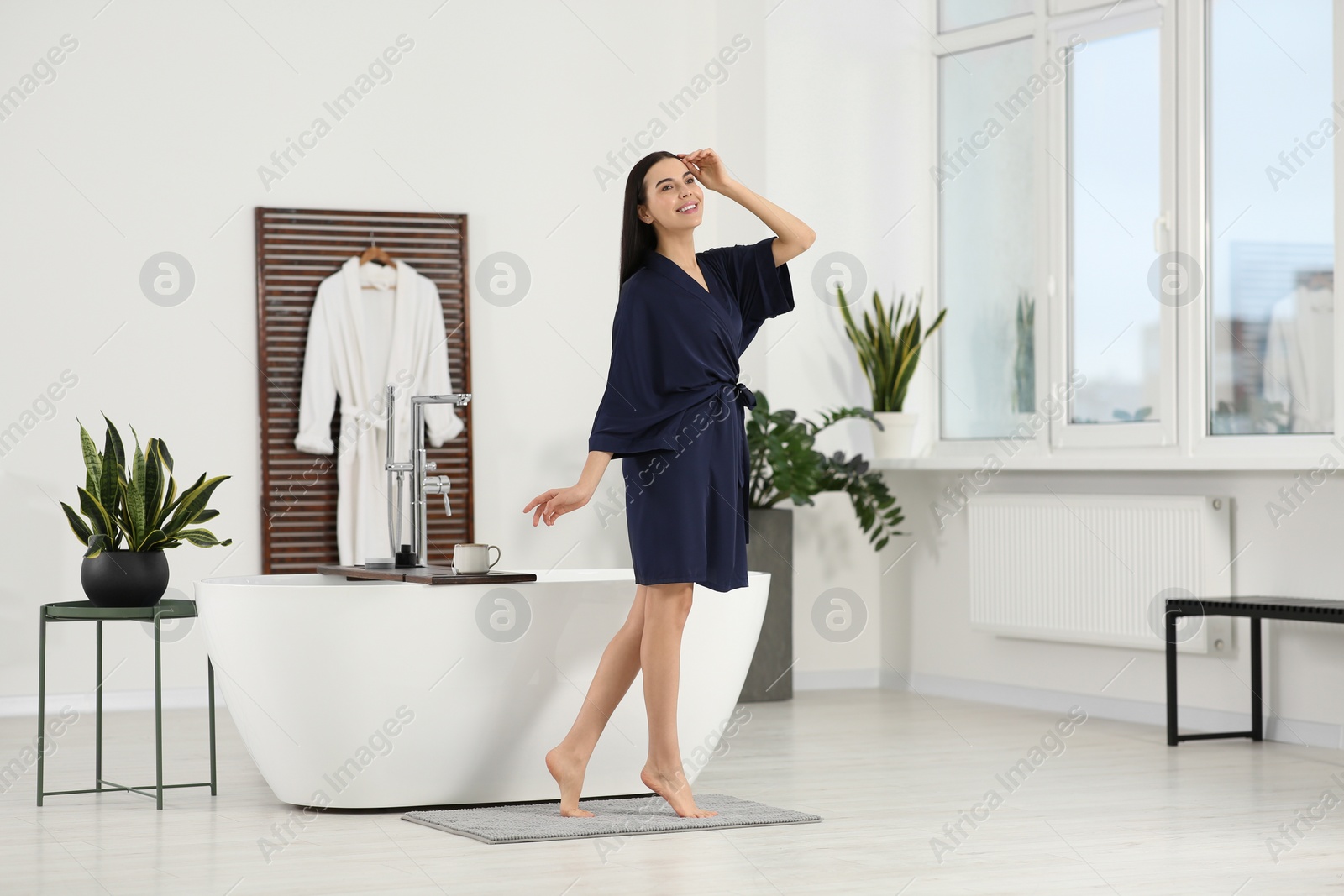 Photo of Beautiful happy woman wearing stylish bathrobe near tub in bathroom