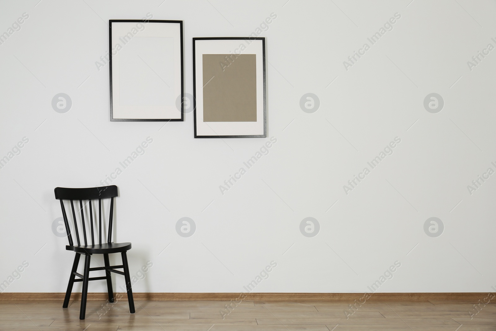Photo of Black chair and frames in room with white wall, space for text. Interior design