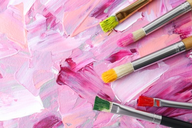 Photo of Set of different brushes on abstract colorful paint, flat lay