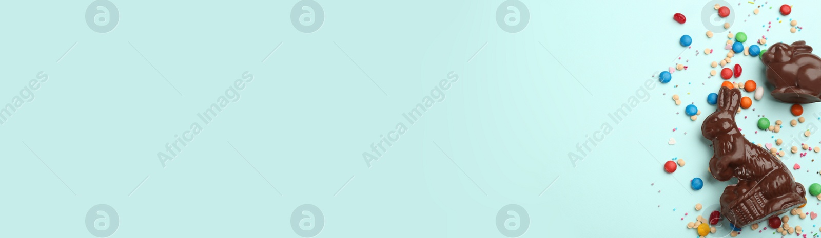 Photo of Flat lay composition with chocolate Easter bunnies and candies on light blue background. Space for text