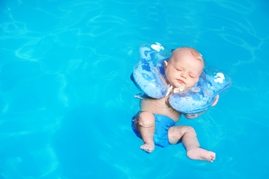 Cute little baby with inflatable neck ring in swimming pool on sunny day, outdoors