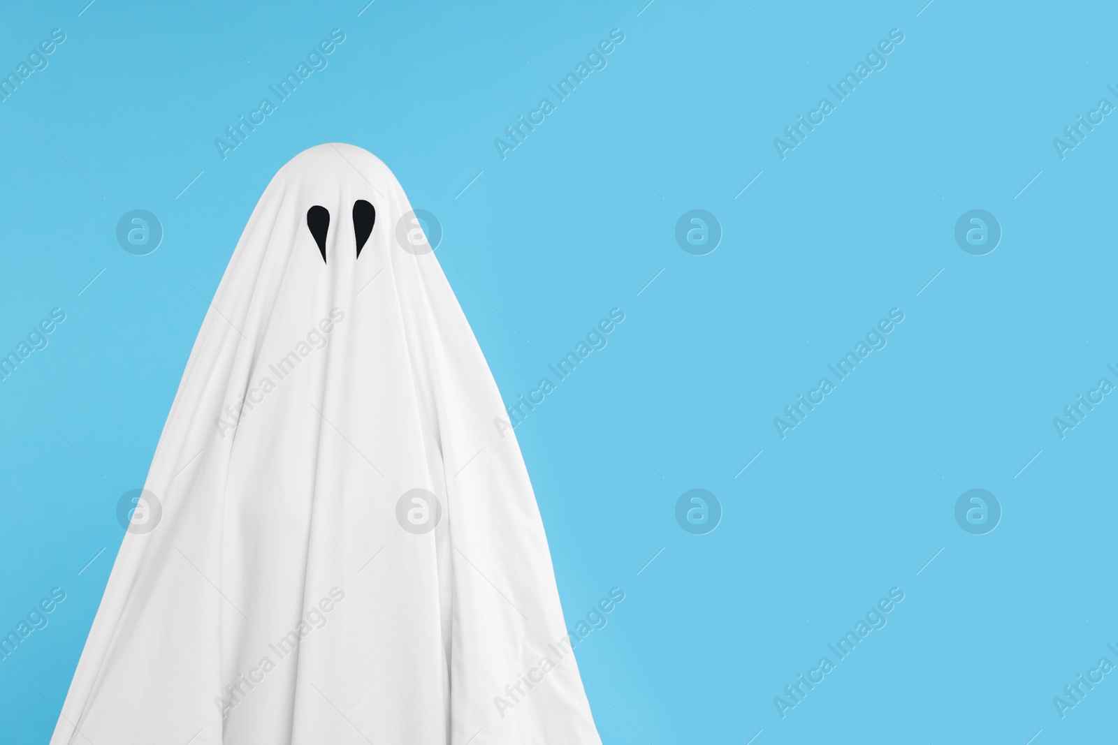 Photo of Woman in white ghost costume on light blue background, space for text. Halloween celebration