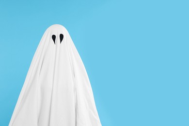 Photo of Woman in white ghost costume on light blue background, space for text. Halloween celebration