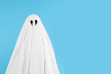 Woman in white ghost costume on light blue background, space for text. Halloween celebration