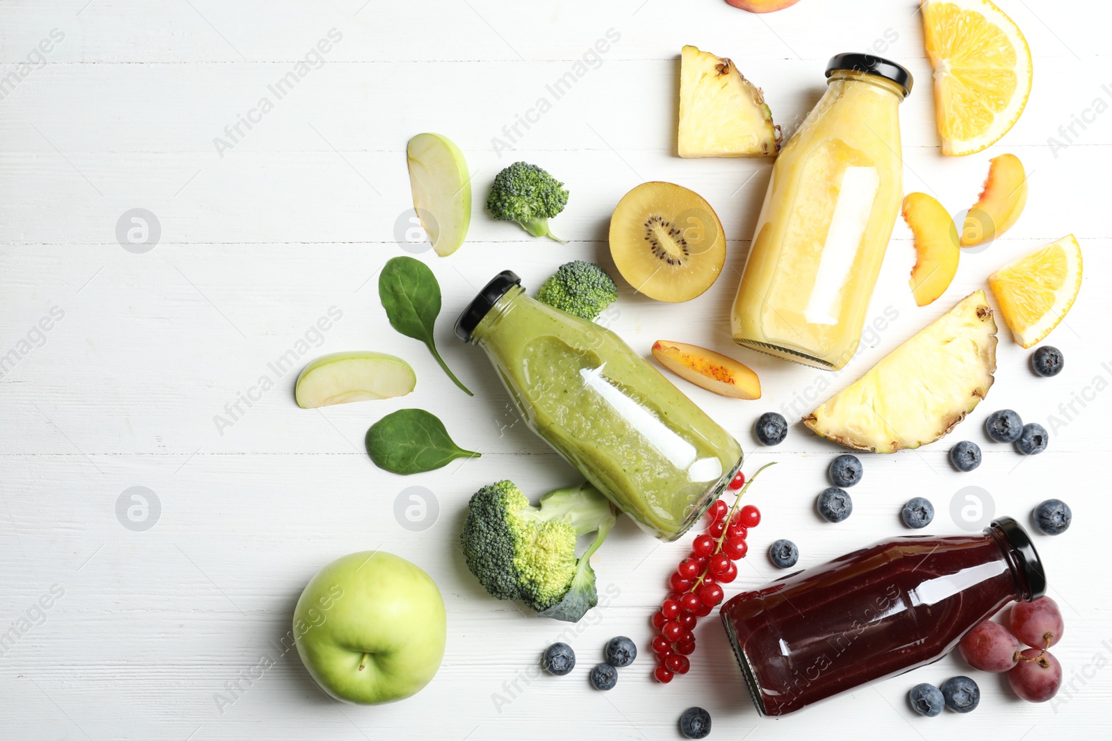 Photo of Bottles of delicious juices and fresh fruits on white wooden table, flat lay