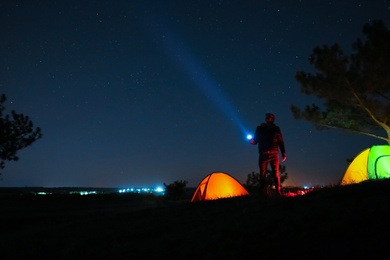 Photo of Man with bright flashlight near camping tents outdoors at night