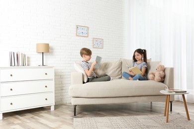 Little boy and girl reading books on sofa at home