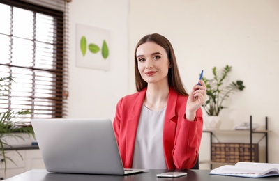 Photo of Young businesswoman using laptop at table in office