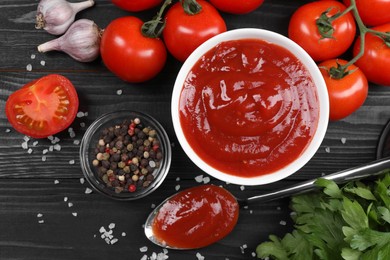 Flat lay composition with delicious ketchup, spices and products on black wooden table. Tomato sauce