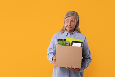 Photo of Unemployed senior woman with box of personal office belongings on orange background. Space for text