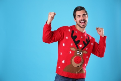 Photo of Happy young man in Christmas sweater on light blue background