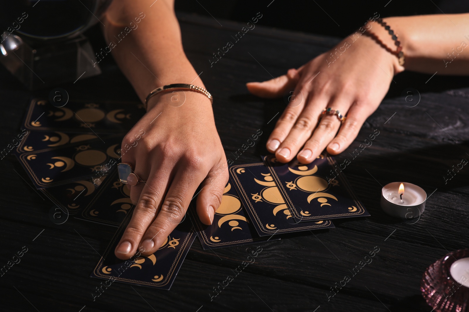 Photo of Soothsayer predicting future with tarot cards at table in darkness, closeup