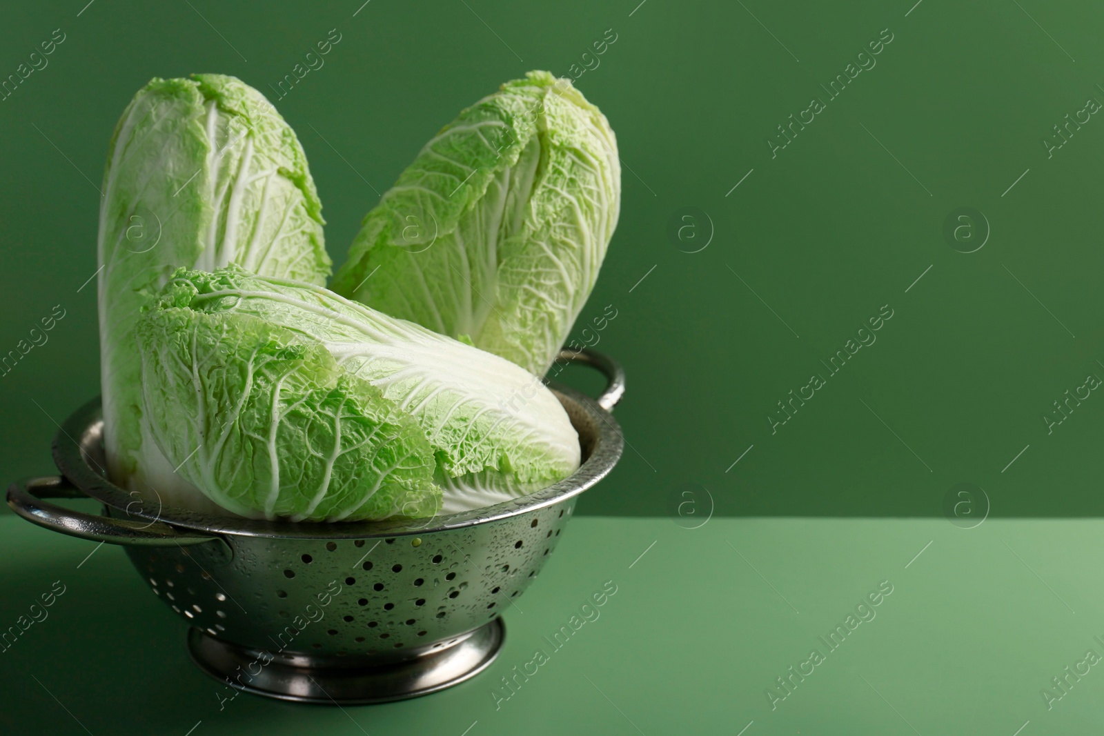 Photo of Fresh Chinese cabbages in colander on green background, closeup. Space for text