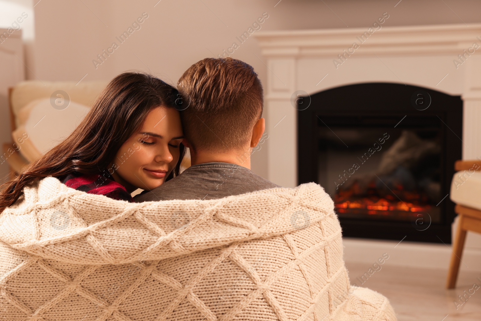 Photo of Lovely couple wrapped in blanket near fireplace at home, back view