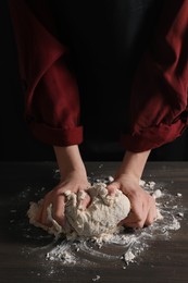 Photo of Making bread. Woman kneading dough at wooden table on dark background, closeup