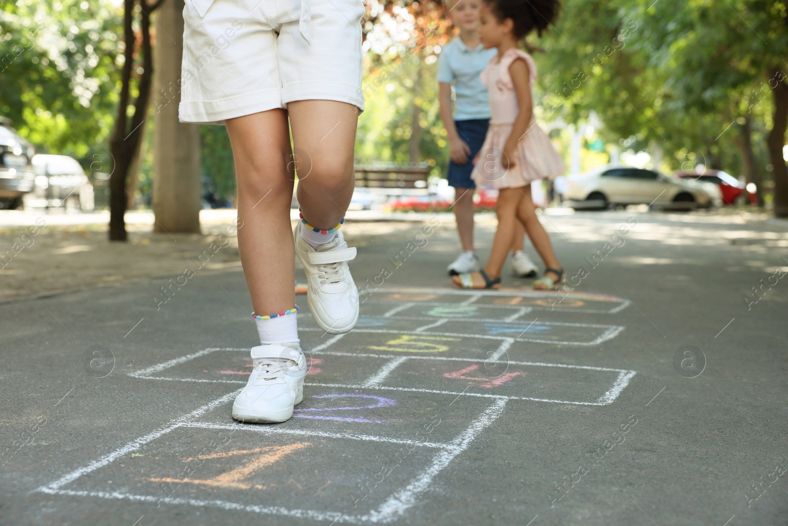 Photo of Little children playing hopscotch drawn with chalk on asphalt outdoors, closeup