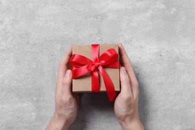 Photo of Man holding gift box with red bow at grey table, top view