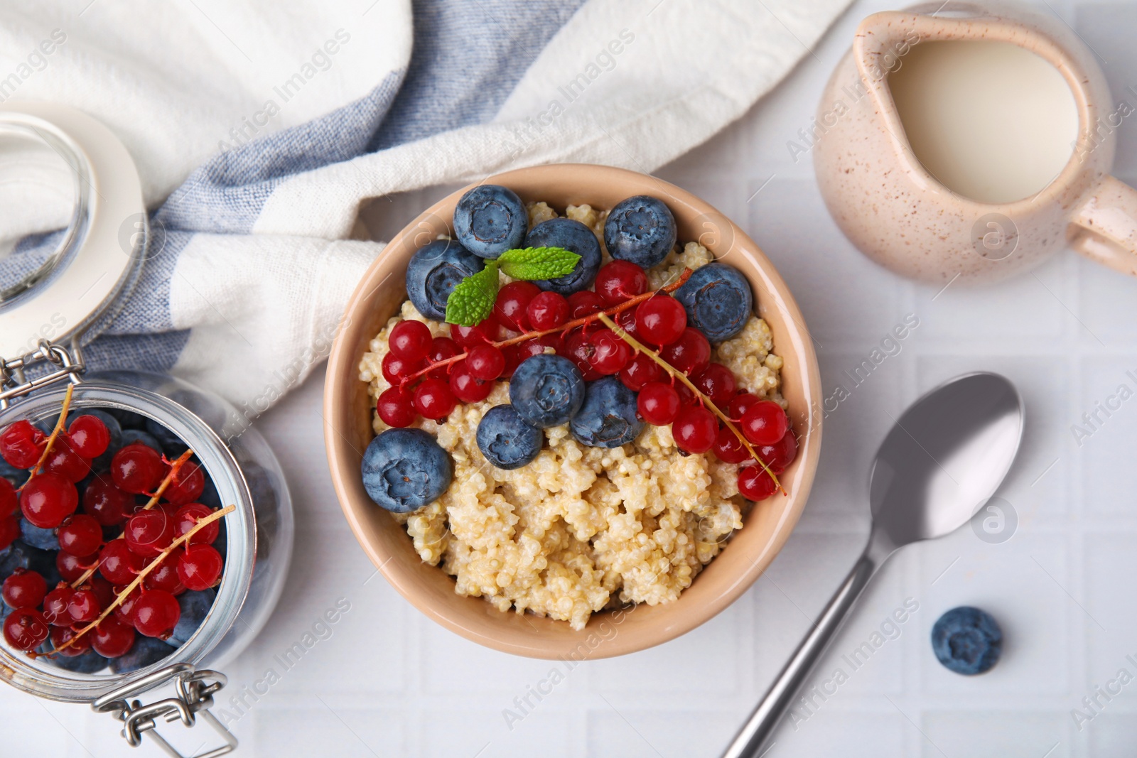 Photo of Bowl of delicious cooked quinoa with blueberries and cranberries on white tiled table, flat lay