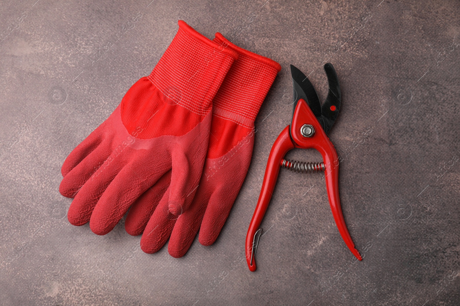 Photo of Pair of red gardening gloves and secateurs on brown textured table, top view
